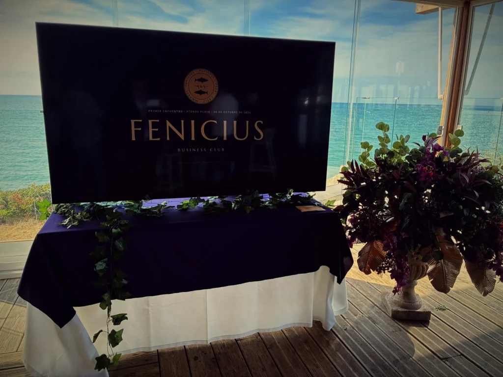 Pantalla con el logotipo de Fenicius Business Club frente al ventanal con el mar de La Barrosa