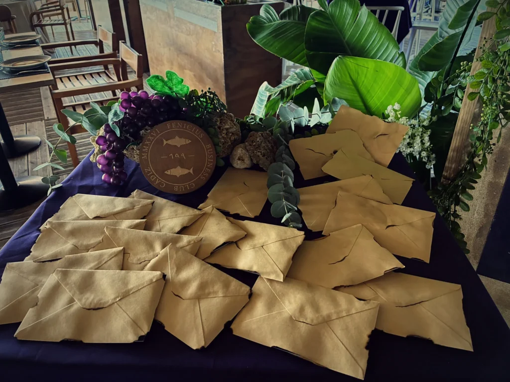 Mesa con sobres de pergamino cerrados y la moneda del club sobre un racimo de uvas